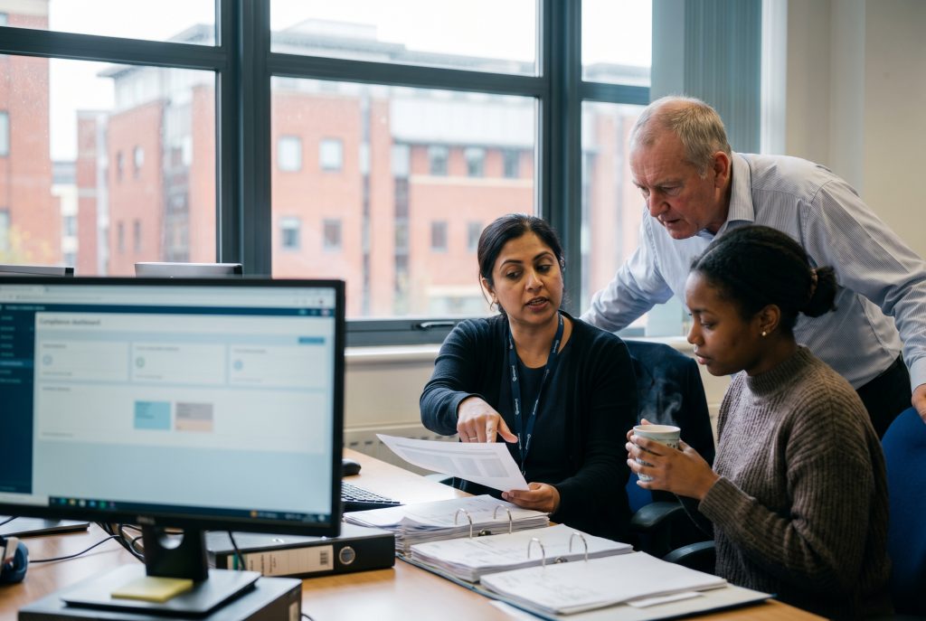 UK payroll team reviewing payslips and a compliance dashboard, illustrating umbrella company compliance