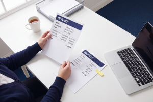 Supply teachers framework invoice held above a supply teacher's payslip on a modern academy office desk with a laptop