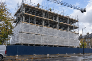 CIS due diligence: scaffolded commercial building under construction, lower lifts hidden by netting, operatives at the top